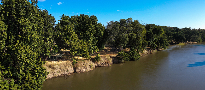 Spacious safari tents line the riverbank, offering unobstructed views of the Zambezi under a clear blue sky.