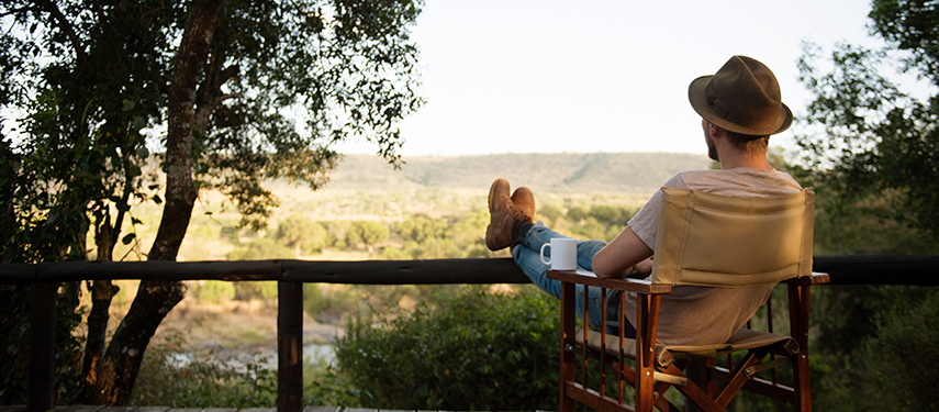 Man relaxes with coffee on the shaded veranda of Serian ‘The Original’, overlooking the lush Mara landscape.