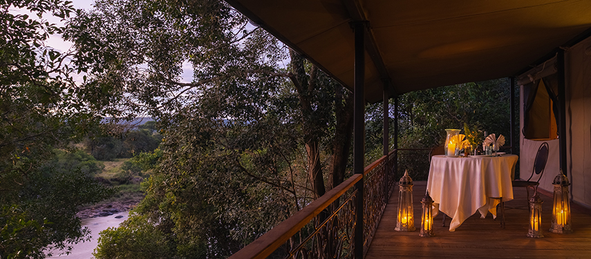 Romantic private dining setup on a tent veranda at Serian ‘The Original’, overlooking the Mara River at dusk.