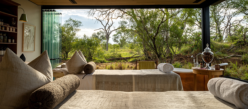 Two treatment beds positioned in front of glass doors offering serene views of the wilderness.