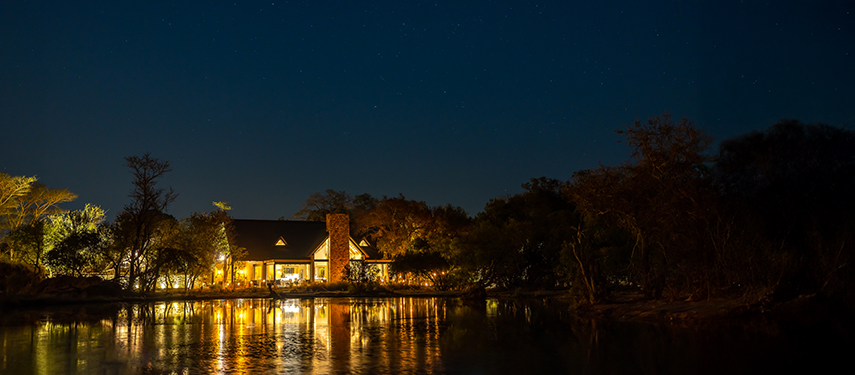 Twilight view of the main lodge exterior, warmly lit with a backdrop of trees and sky.