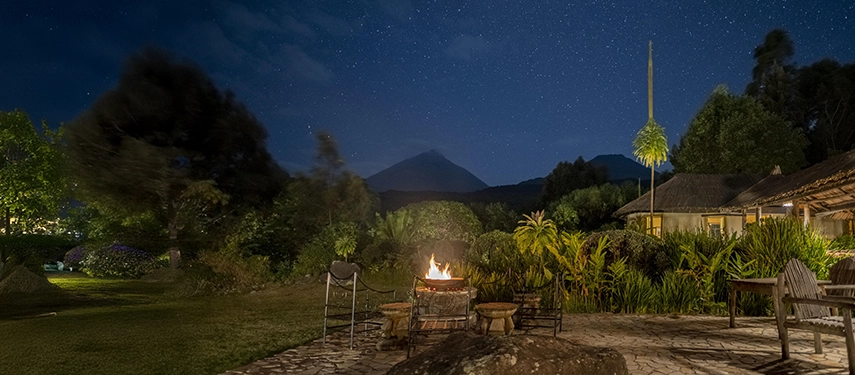 Fire pit glowing under a starry night sky with views of Mount Gahinga and the lodge’s peaceful garden.