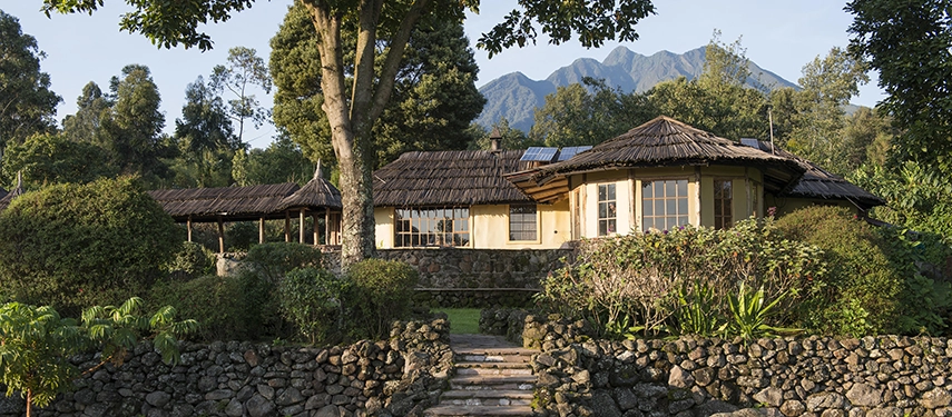 Exterior view of Mount Gahinga Lodge with volcanic peaks rising in the background and lush gardens in the foreground.