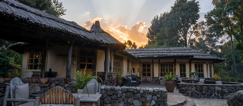 Sunset casting golden light over the stone terrace and traditional bandas of Mount Gahinga Lodge.