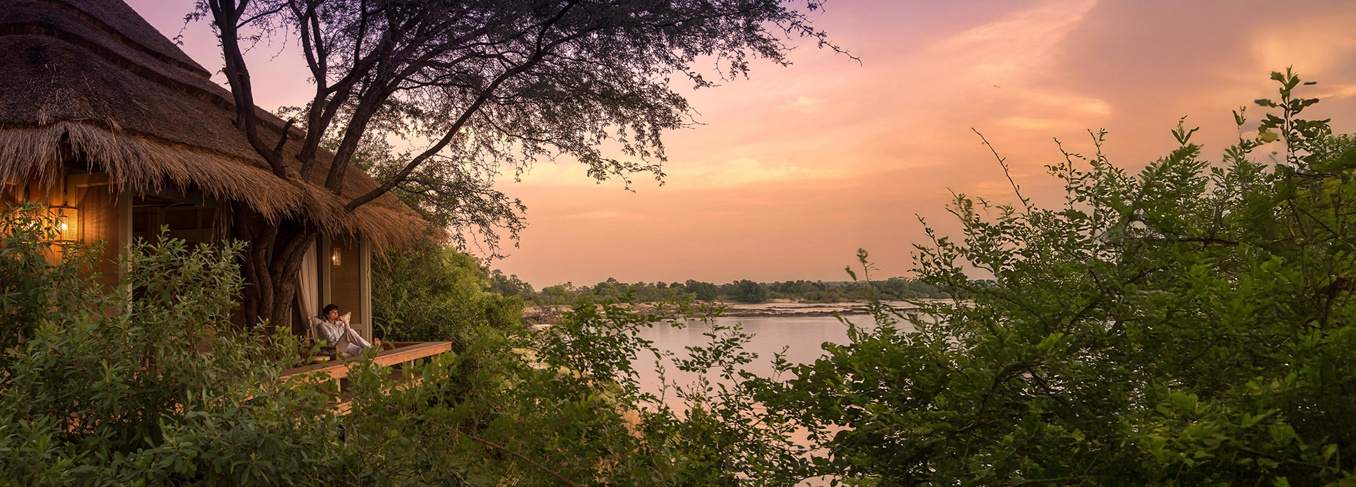 A luxury suite at Mpala Jena overlooking the Zambezi River at sunset, with a private deck framed by riverine forest and calm waters flowing past Mana Pools.