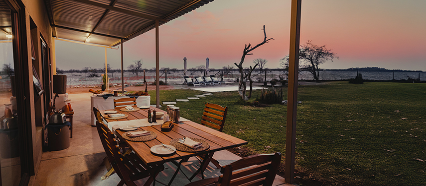 Outdoor dining table set for dinner on the covered veranda at Safari House during sunset.