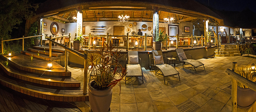 Ngoma Safari Lodge lit warmly at night, showcasing the open-air lounge and dining space with inviting lanterns.