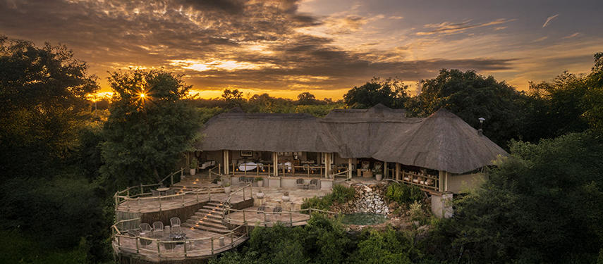 Thatched main lodge of Ngoma Safari Lodge captured at sunset with tiered decking and surrounding forest.