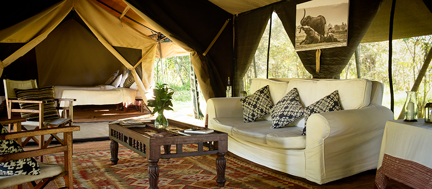 Inside view of a canvas tent at Nkorombo with armchairs, a double bed, and stylish safari decor.