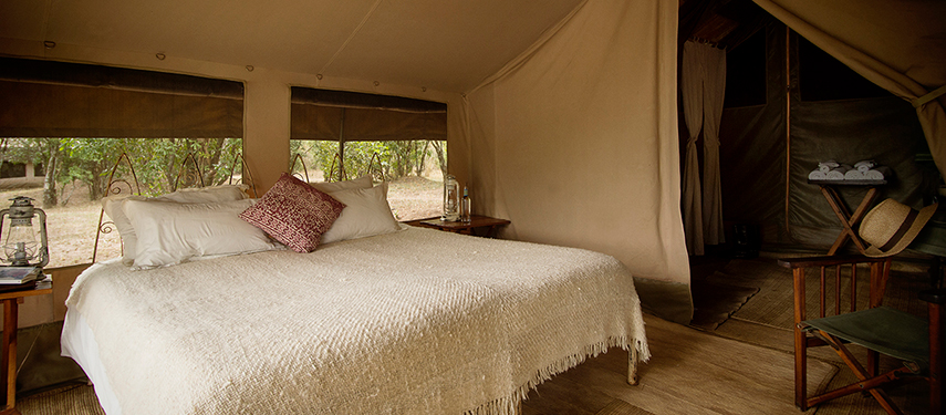 A warmly lit canvas bedroom at Nkorombo Mobile featuring a king bed, lanterns, and rustic furnishings.