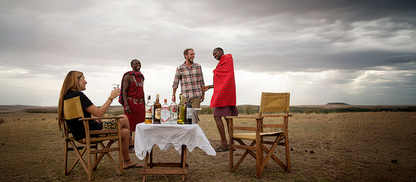 A private sundowner setup on the open plains with drinks, Maasai hosts, and sweeping views.