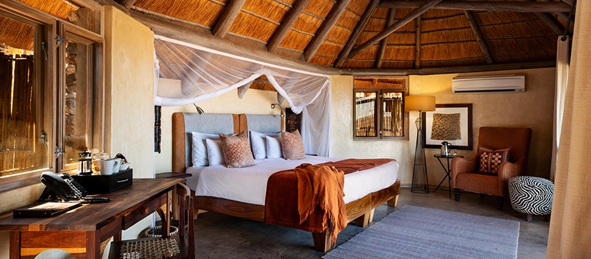 legant thatched suite at Ongava Lodge featuring a mosquito-netted bed, earthy tones, and traditional wooden furnishings.