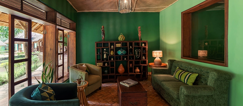 Reception area at Primate Lodge Kibale with earthy green walls, wooden shelving, and comfortable sofas.