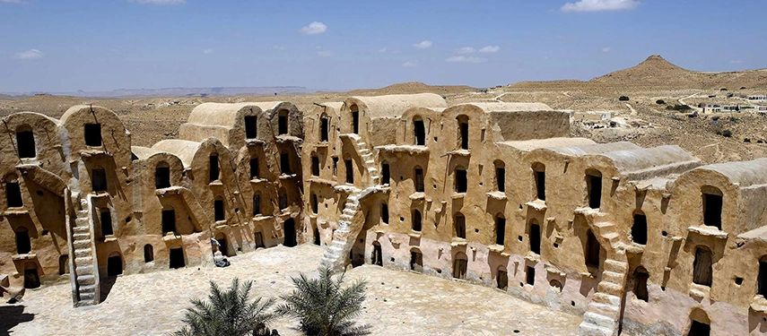 Ancient ksar granary buildings with arched facades and desert mountains in the background near Douz.