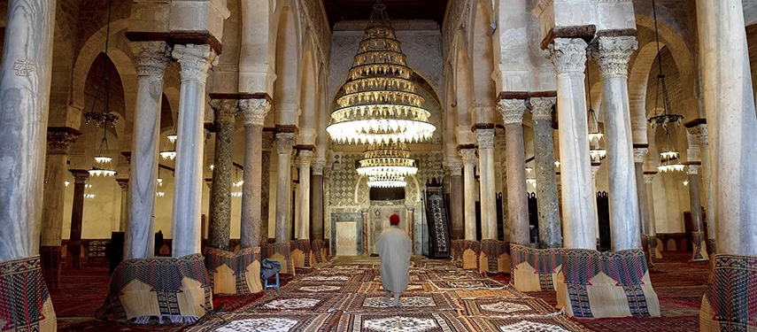Interior of Kairouan’s Great Mosque featuring ornate chandeliers, arches, and richly patterned carpets.
