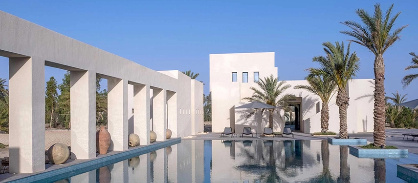 Modern infinity-style pool at The Residence Douz surrounded by palm trees and white stone architecture.