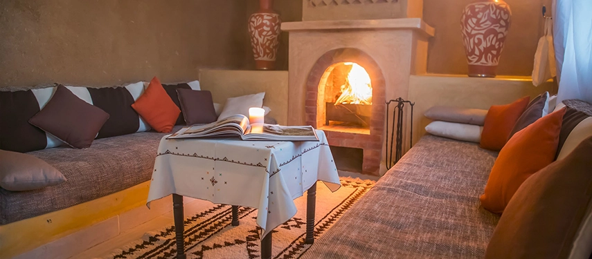 Cosy lounge with cushioned seating, warm lighting, and a fireplace creating a welcoming Moroccan atmosphere.
