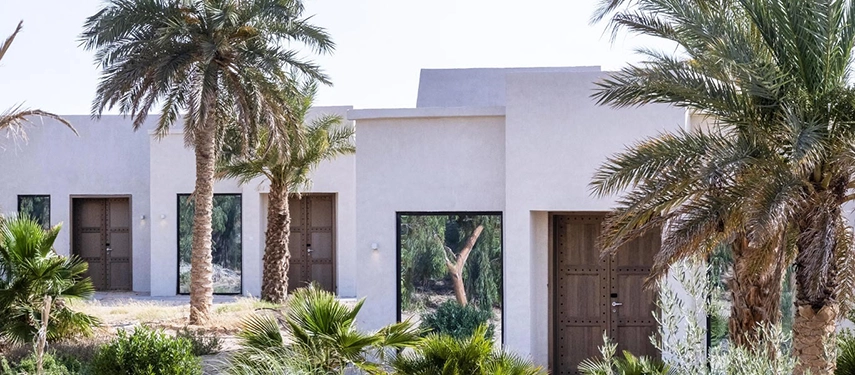 Exterior of guest villas at The Residence Douz framed by palm trees and desert landscaping.