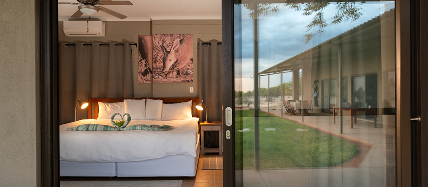 View through sliding doors of a Safari House bedroom with a king-size bed and courtyard lawn outside.