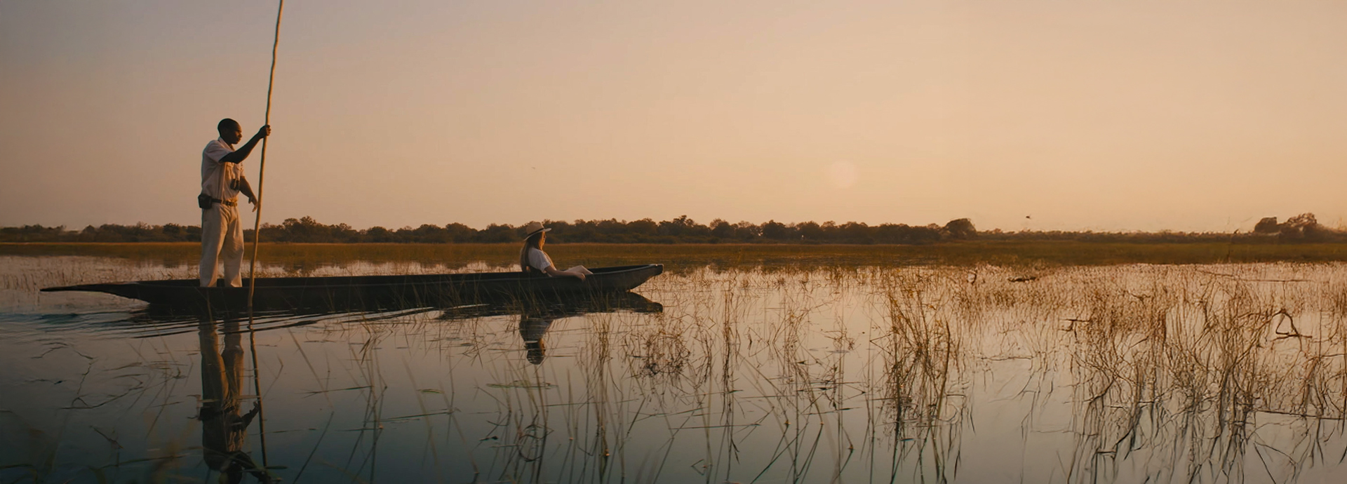 Guests on a traditional mokoro canoe safari at sunset, paddling through reeds in the Okavango Delta with a local guide.
