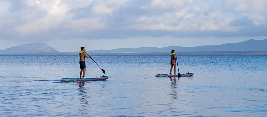 Guests paddleboarding in calm Galápagos waters near the Hermes Galápagos Mega Catamaran.