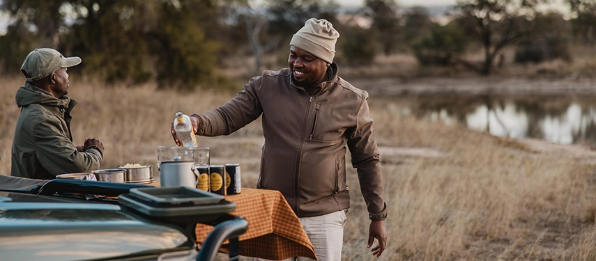 A guide pouring drinks for guests during a morning game drive coffee stop in the bush.