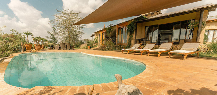 Sun loungers and a shaded terrace overlook a turquoise pool in front of the main lodge at The Emakoko.
