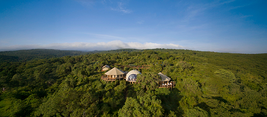 Aerial view of The Highlands camp surrounded by lush green forest and volcano slopes