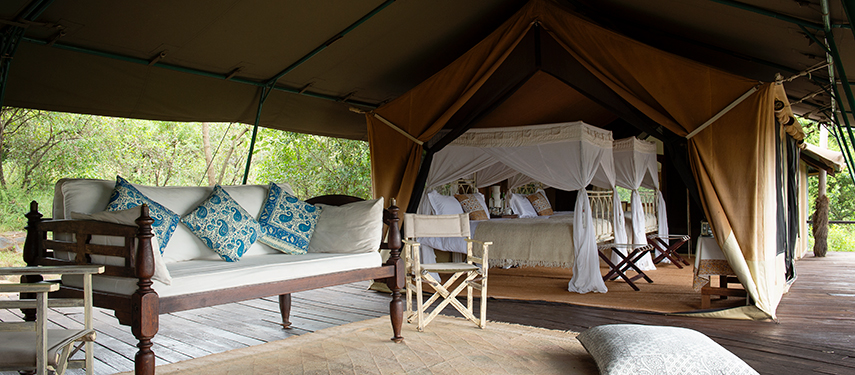 Open-fronted tented suite with elegant four-poster bed, vintage-style furnishings, and a shaded wooden deck at Serian ‘The Original’.
