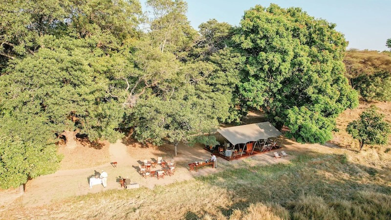 An aerial view of Time + Tide Luwi Camp in South Luangwa National Park, showing the intimate riverside dining area tucked beneath mature trees.