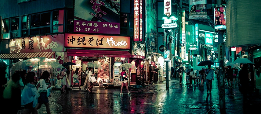 A lively Tokyo street at night glowing with neon signs and reflections on wet pavement, showcasing the city’s vibrant urban energy.