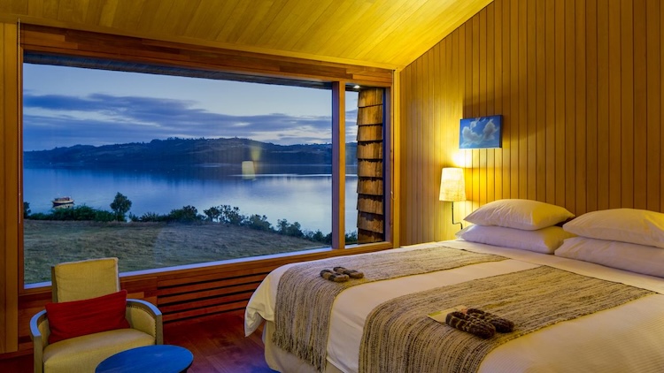 A warmly lit guest room at Refugia Lodge with expansive views of the bay at dusk