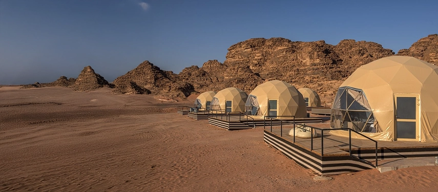 Geodesic desert domes sit on raised decks amid the vast red sands and sculpted rock formations of Wadi Rum.