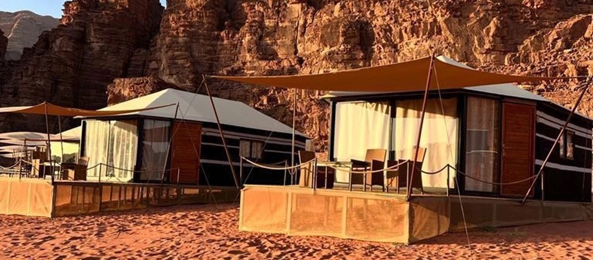 Luxury desert tents with shaded terraces sit beneath dramatic rock faces, blending into the warm tones of the surrounding sands.