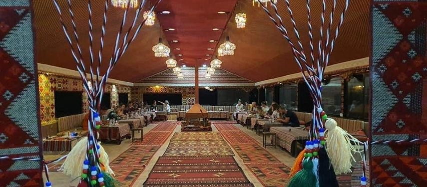 The dining tent is richly decorated with traditional Bedouin textiles and lanterns beneath a starlit desert sky.