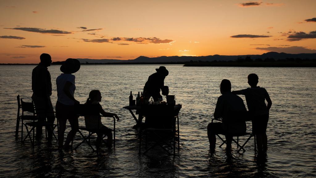 Guests enjoying sundowners in shallow Zambezi River waters during sunset near Tembo Plains Camp in Sapi Reserve, Zimbabwe.