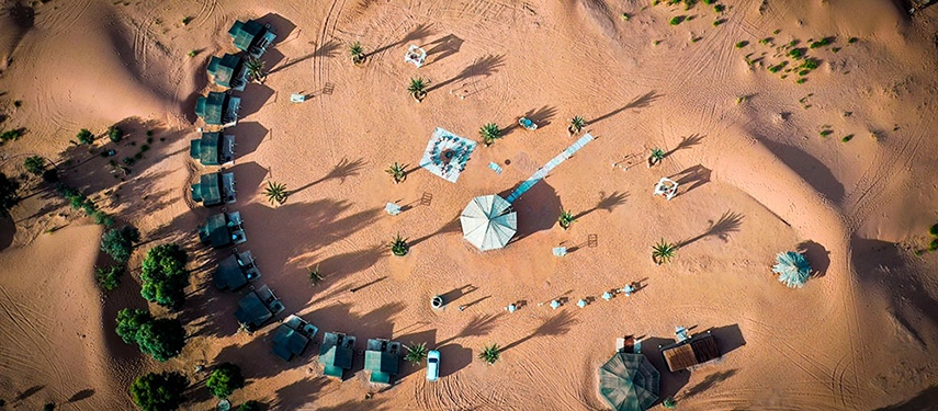 Drone view of Riad Madu camp layout with tents, palm trees, and desert landscape stretching into the horizon.