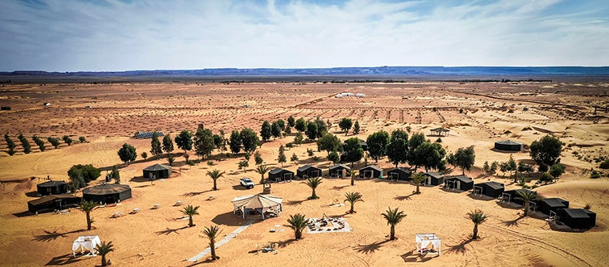 Drone view of Riad Madu camp layout with tents, palm trees, and desert landscape stretching into the horizon.
