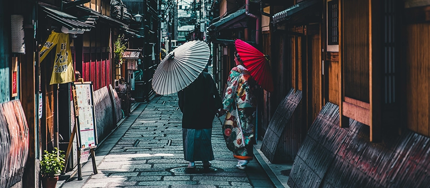 Two figures in traditional dress walk along a narrow lantern-lit street in Kyoto, reflecting the enduring spirit of old Japan.