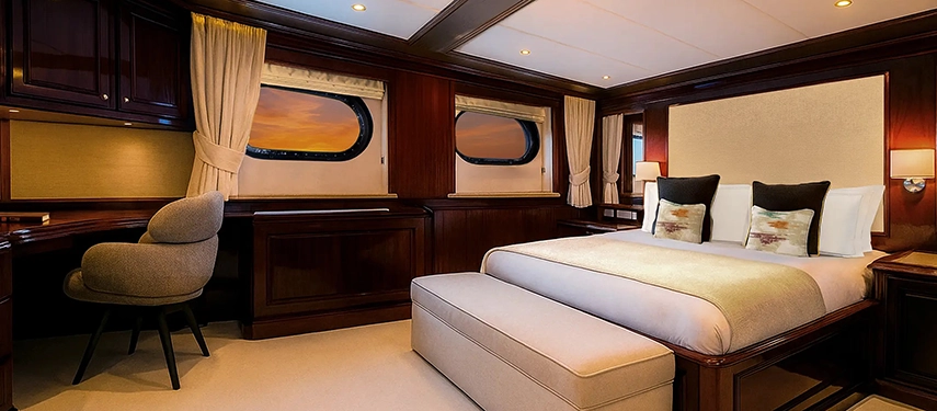 Warmly lit cabin with polished timber finishes, ocean-view windows and a writing desk.