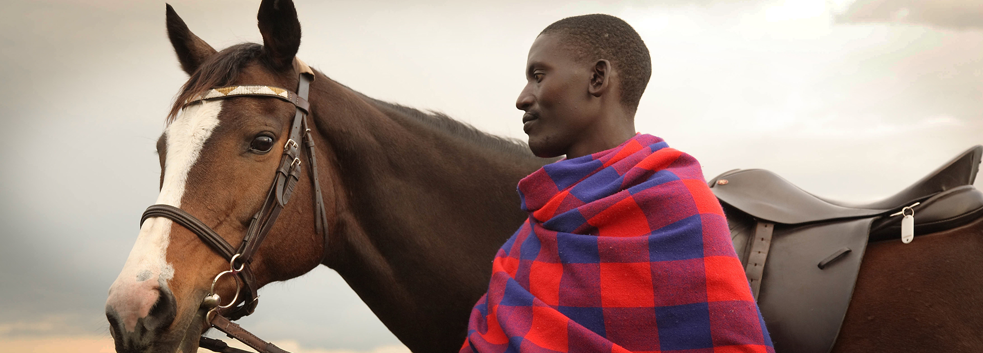 A Maasai tribesman stands with a horse on an African riding safari