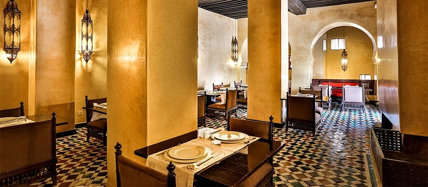 Atmospheric dining room at Dar Bensouda with Moroccan lanterns, tiled floors, and intimate alcove seating.