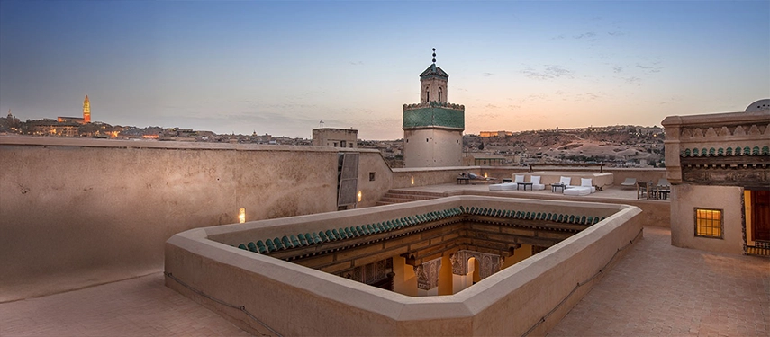 Rooftop view from Dar Bensouda at dusk, showcasing a green-tiled minaret and the Fes skyline.