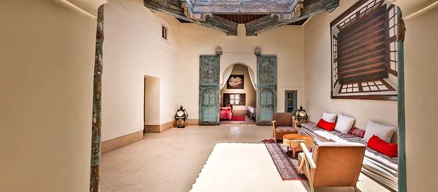 Elegant lounge space at Dar Bensouda with traditional doors, soft seating, and an adjoining bedroom beyond.