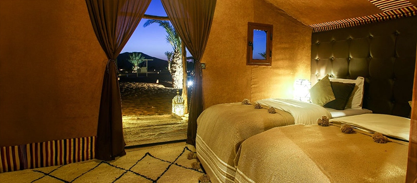 Twin bed tent interior with warm Moroccan textiles and a view out to the desert night.