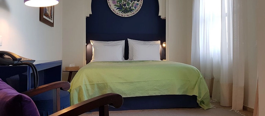 Elegant bedroom with a deep blue headboard, lime green bedspread, and soft natural light filtering through white curtains.