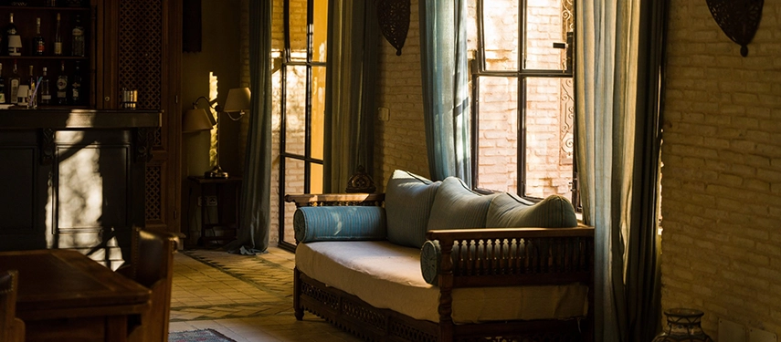 Serene lounge at Dar Tozeur with soft natural light, a wooden sofa, and flowing curtains.