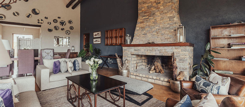 A cosy lounge area at The Emakoko featuring a stone fireplace, plush sofas, and African-inspired decor.