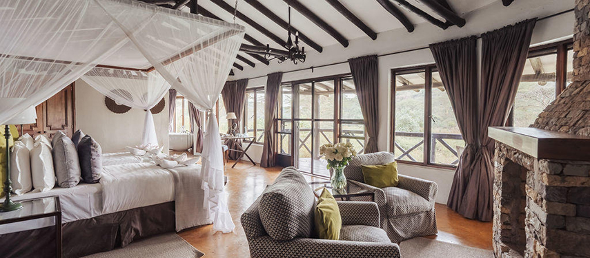 An elegant guest suite at The Emakoko with a four-poster bed, armchairs, and large windows looking out to the gorge.