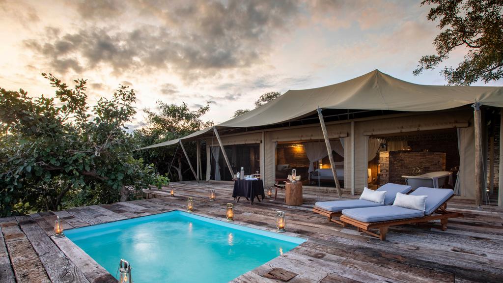 rivate safari tent with plunge pool and wooden deck at Tembo Plains Camp in Sapi Reserve, Zimbabwe, overlooking the surrounding bush at sunset.